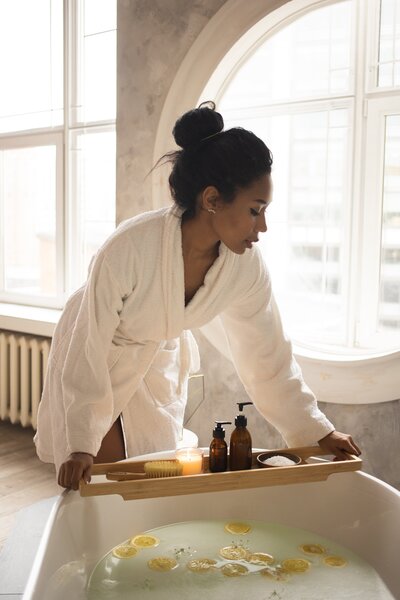 A woman in a white robe setting up a bath with floating citrus slices, creating a refreshing and luxurious self-care experience with natural elements.