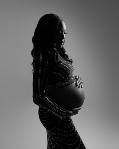 pregnant black woman wearing fitted, black maternity gown with open belly and sparkles in moody lighting.