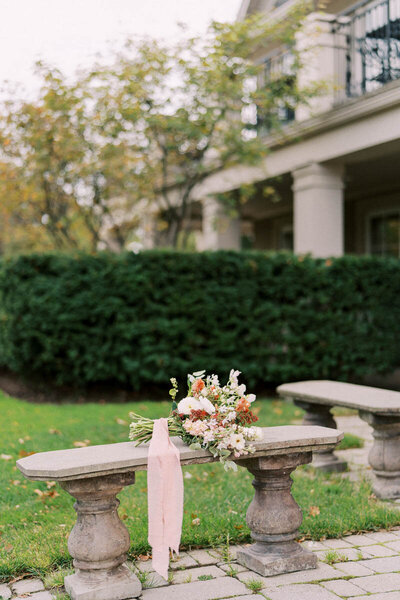 Wedding bouquet with pink ribbon laid on stone bench in garden at Oakville Golf Club