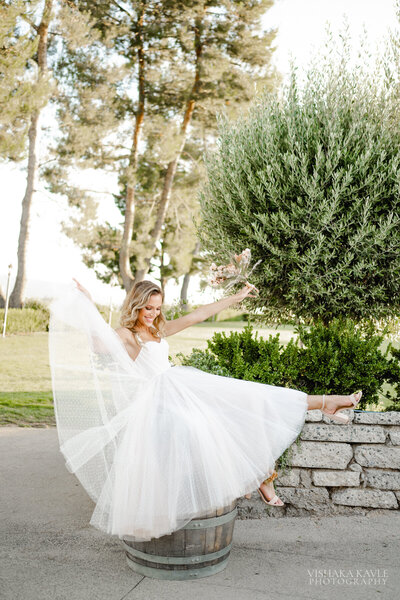 bride sitting on a barrel while laughing and kicking her feet
