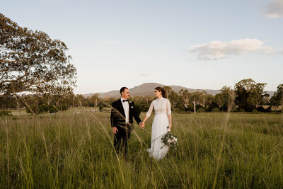 Couple hold hands looking at each other in a field with mountains in the background - Mount Tamborine Wedding photographer