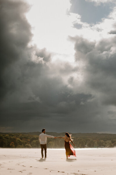 Two people reaching out and holding hands while walking in the sand 