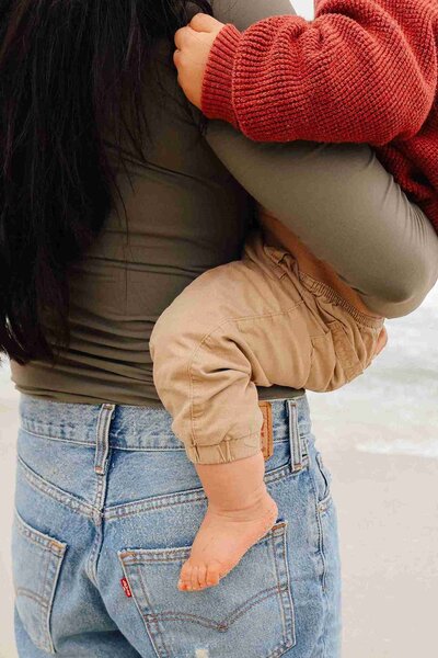 A woman joyfully carries a baby on her hip during a family photography session, capturing their special bond.