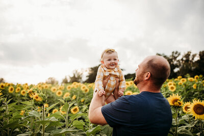 Man holding baby in yellow shirt in field of sunflowers in Jarrettsville, Maryland