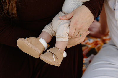 A baby's shoes in the arms of his mother as they share a loving embrace