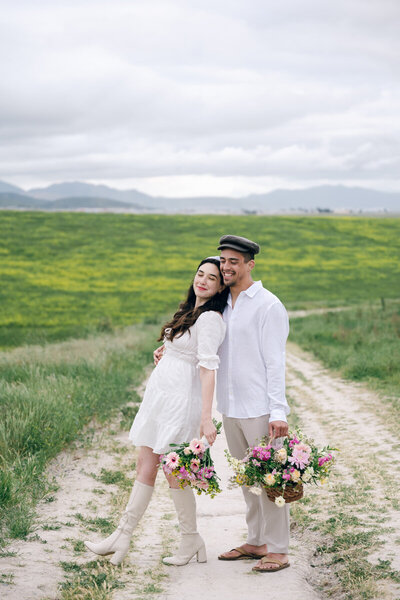 man and woman standing in a field holding flowers with mountains in the background