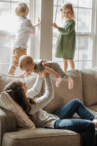 Lifestyle family picture of a mom playing with her baby on the couch, while two toddlers climb on the back. Captured by San Antonio family photographer Cassey Golden.