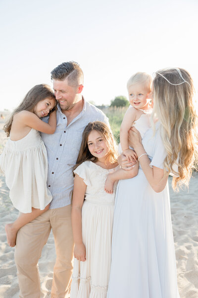 Parents smile with their three children during sunset family portrait session at Sherwood Island beach