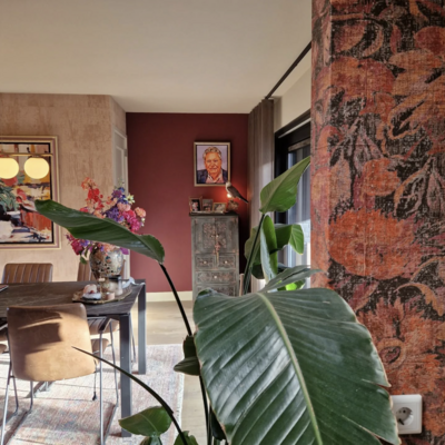 Interieur met warme rode muren, kleurrijk bloemstuk en portretkunst, gezien vanuit de woonkamer