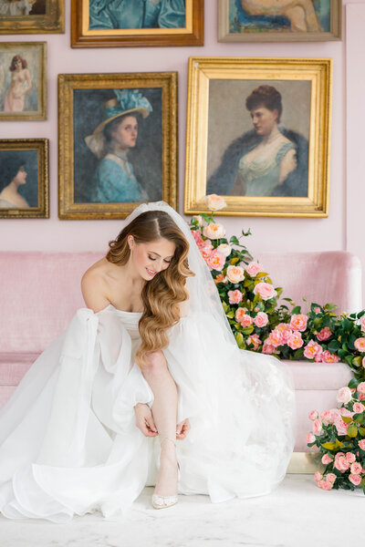 Wedding Videography in Newport, CT, RI, and beyond | The Corteses | Bride with an off the shoulder gown fixing her heels while sitting on a pink couch