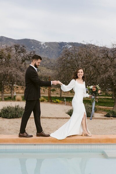 bride and groom holding hands walking at the edge of pool outside mountain background taken by st paul wedding photographer tom thornton
