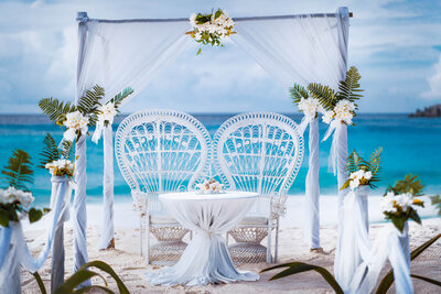 Romantic beach wedding setup with white chairs, floral decorations, and an ocean backdrop.