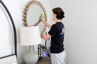 Professional cleaner wiping down a mirror in a bedroom