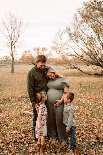 family with expecting mother standing in a field in the fall