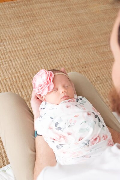 Small newborn swaddles in a flower blanket with a big pink flower headband.