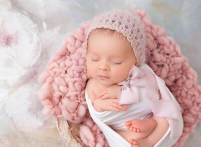 Rochel Konik Photography | Top NYC Brooklyn Newborn Photographer captures sleeping baby girl wrapped in a pink wrap atop pink tulle. her hands are toes are exposed and one hand resting under her chin.