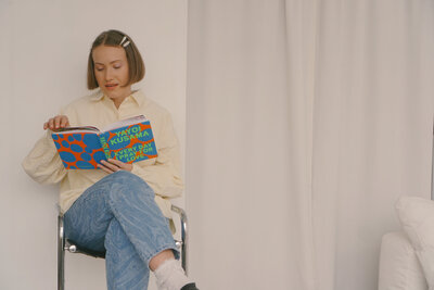 Margarita is reading a book titled "every day I pray for love" while siting on a stool against a white wall. Harvesting inspiratiosn for ethical marketing ideas.