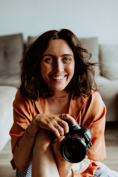 female photographer sitting with camera smiling