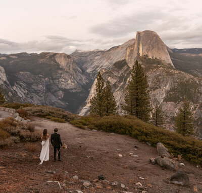 A couple holds hands and walks with an incredible mountain with orange alpenglow behind them during their elopement in Montana.