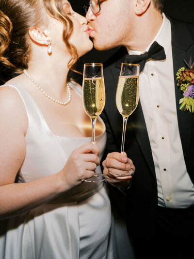 A couple kisses, cheersing two glasses of champagne during their wedding reception in Tulsa, Oklahoma.