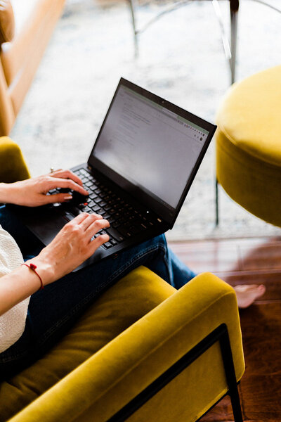 woman on laptop on mustard colored chair