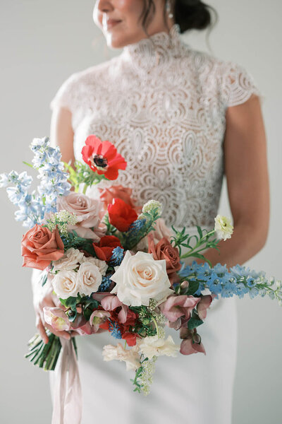 Bride holding a colorful wedding bouquet with red anemones, white roses, dusty pink garden roses, and blue delphinium for a luxury wedding at the Kimpton Armory.
