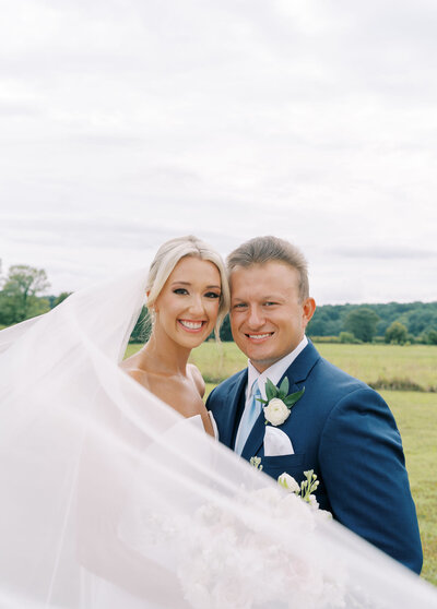 a bride and groom embracing while standing in a field
