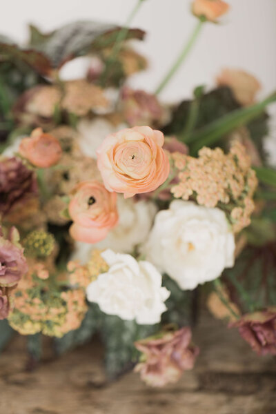 A close-up of a floral arrangement with peach ranunculus and white roses.