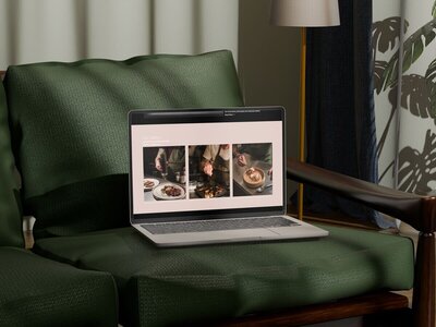 Laptop showing a restaurant website design gallery page with plated dishes. on a green luxury sofa