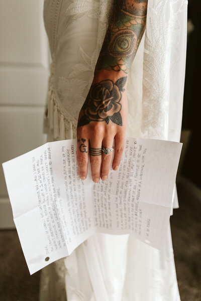 close up of a tattoo hand holding handwritten vows on wedding day