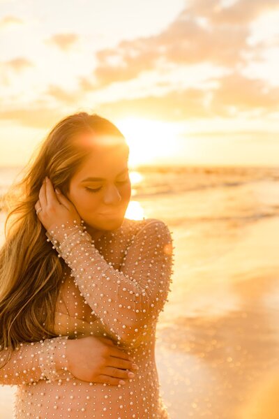 wind blows hair behind the ear of a pregnant woman wearing a long gold sequined maternity gown