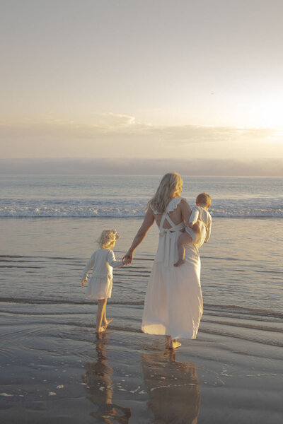 Mother walking on the beach with her two children at sunset