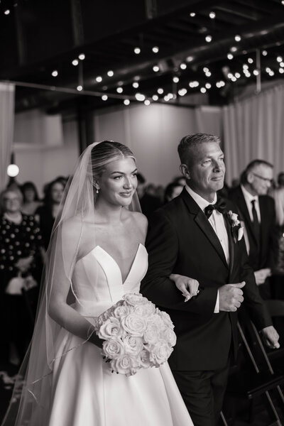 A bride getting ready in a white robe applies makeup in a mirror, surrounded by flowers and decorative items, creating a calm, intimate atmosphere.