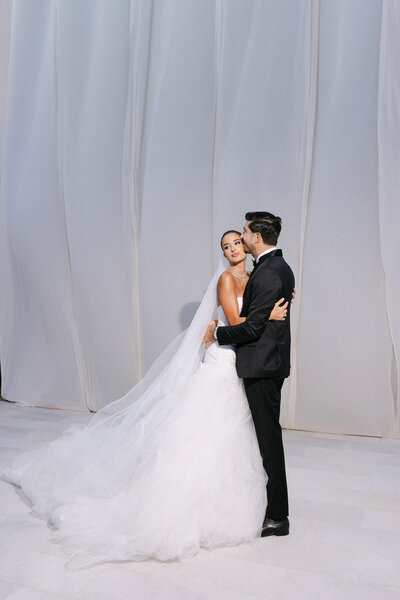 Celebrity model Julia Hussein hugging her husband in from of a white draped backdrop.