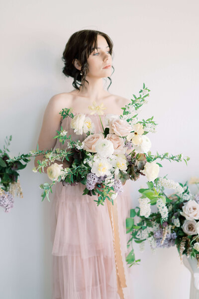 bride holding large floral bouquet of dusty pink, white and lavender florals with greenery