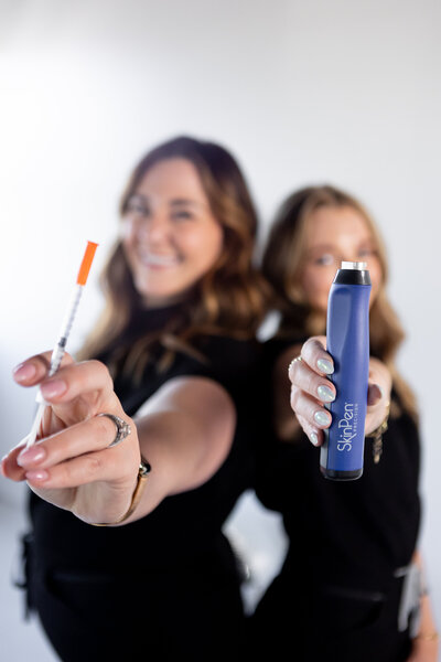 girls holding a skin pen microneedling tol and a syringe of botox
