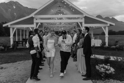 Wedding couple runs through confetti in black and white send-off.
