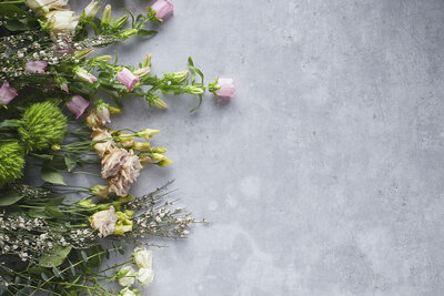 Soft-toned flowers and greenery laid out on a gray surface