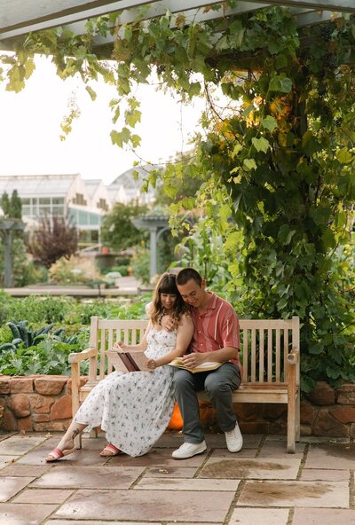 Couple reading a book on a bench under lush greenery at the Denver Botanic Gardens during their engagement photos 