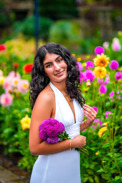 A Liberty High School senior is standing in front of colorful dahlias at Point Defiance Rose Garden for her senior photos with Mikayla Arsenian Photography. 