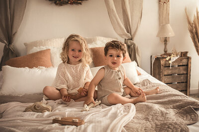 Frère et sœur en tenue bohème assis sur un lit tissu lin