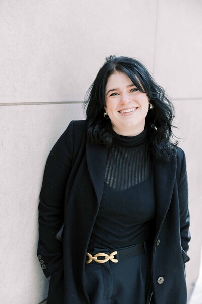 The wedding photographer, smiling while holding an instant camera, dressed in a pale blue robe with feathered sleeves.