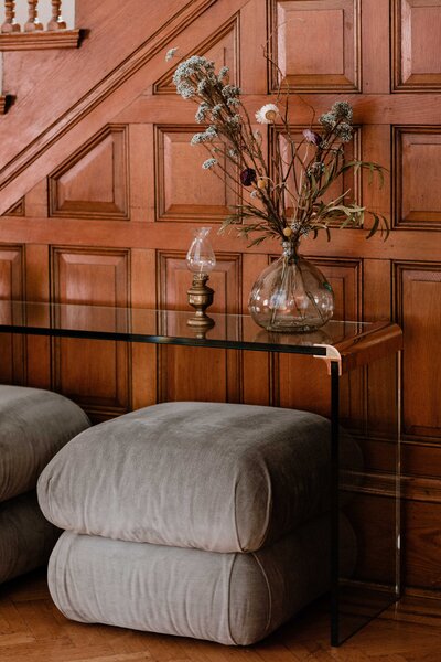 An acrylic console table in front of a wood-paneled wall with two ottomans beneath