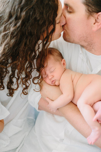 New parents kiss as the farther holds their newborn baby