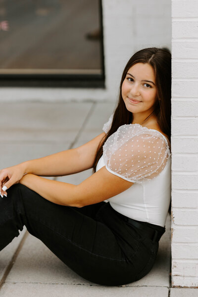 Senior girl leaning against a wall and soft smiling at the camera