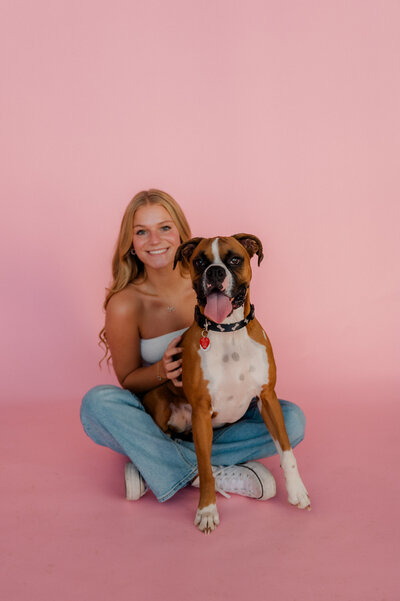 Teen girl smiles with her dog in front of pink backdrop at Studio 125.