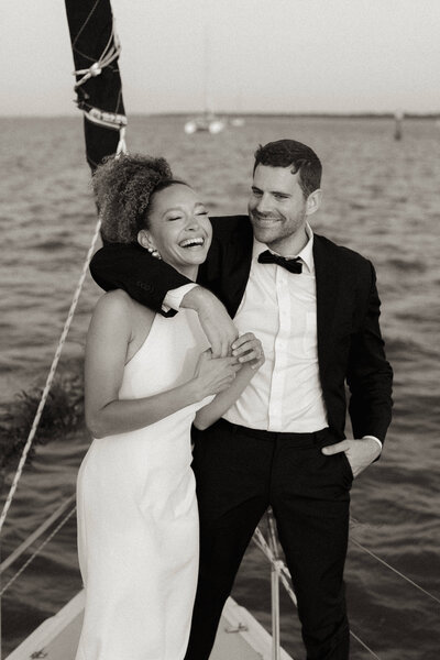 A bride and groom laughing on a sailboat in Charleston.