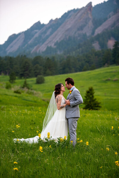 A bride and groom dance in a grassy field with yellow flowers with the Boulder Flatirons in the background.