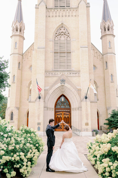 groom twirling bride in front of a cathedral on their wedding day