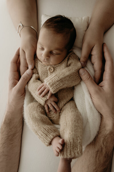 Close-up of an adult's hands gently holding a newborn's feet, with the newborn lying down in the background, captured beautifully during a Wollongong motherhood session.
